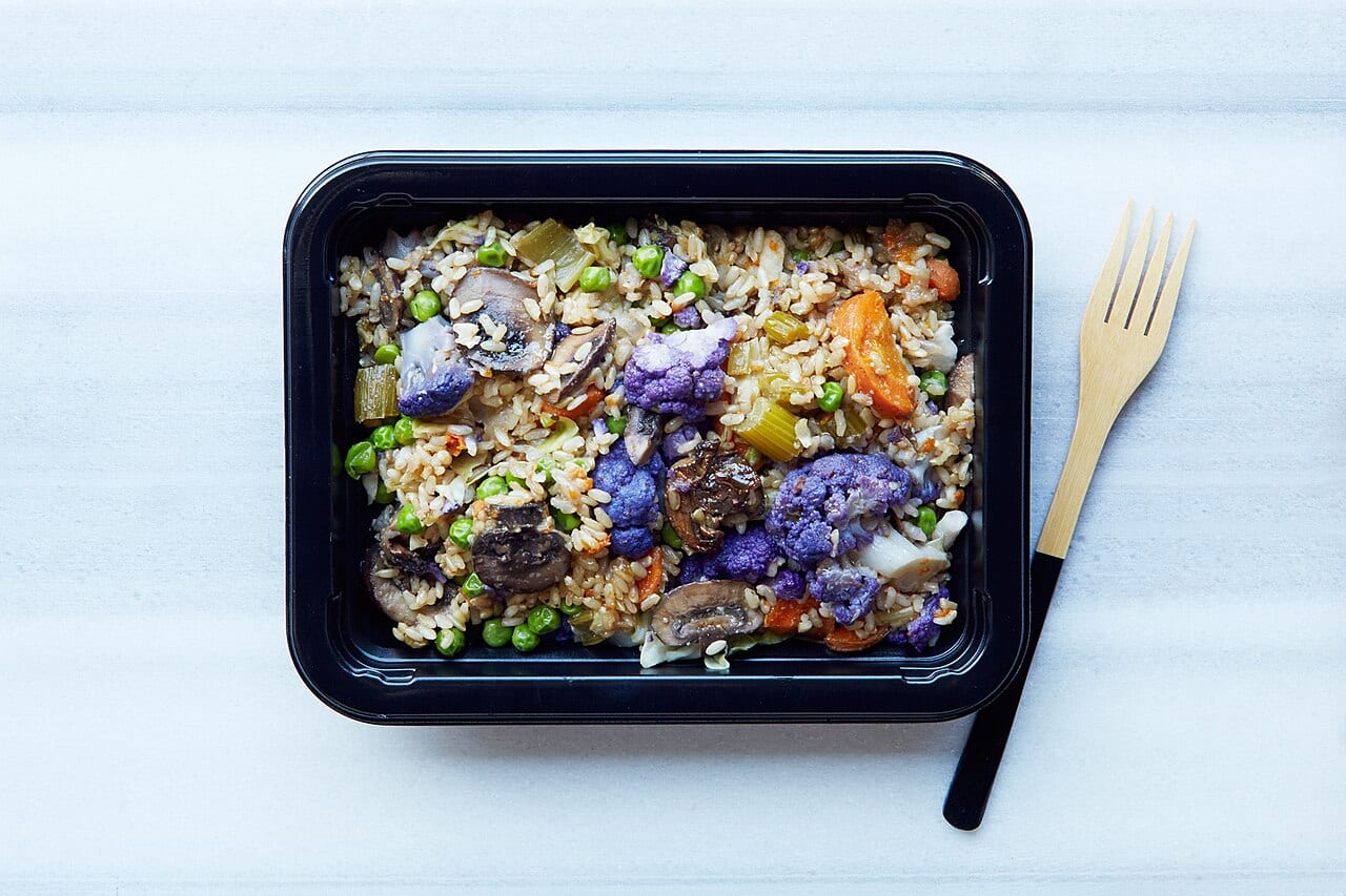 A plant-based meal sits ready in a clear plastic meal prep container