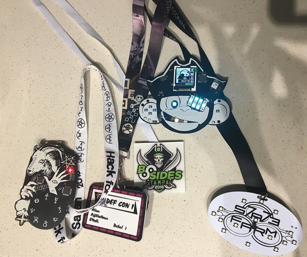 A row of electronic and paper badges from hacker conferences