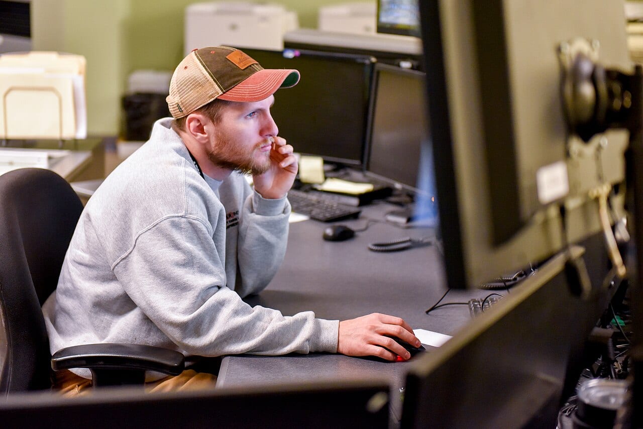 An operator in a control room watches a bank of computer screens for problems