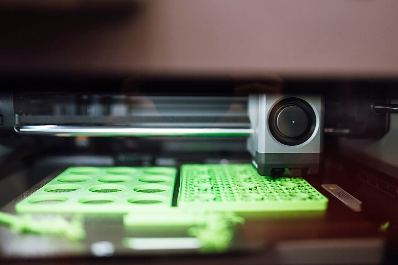 A desktop 3D printer laying down green plastic parts on its bed