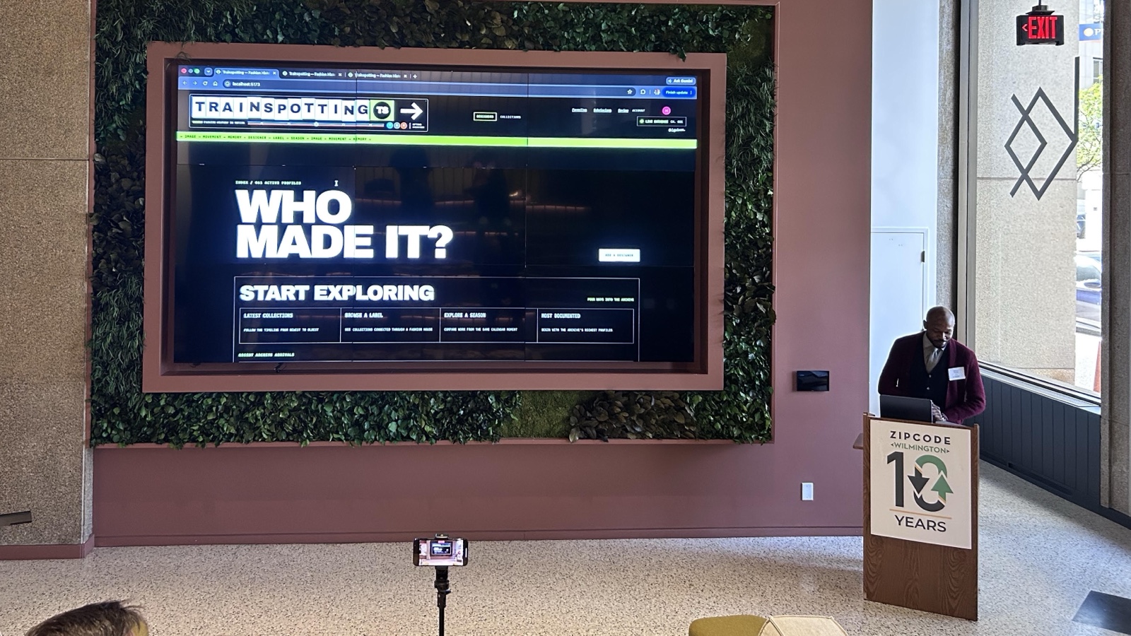 Hakeem Gaines at a Zip Code Wilmington podium, with Trainspotting's home page on a wall-size screen beside him