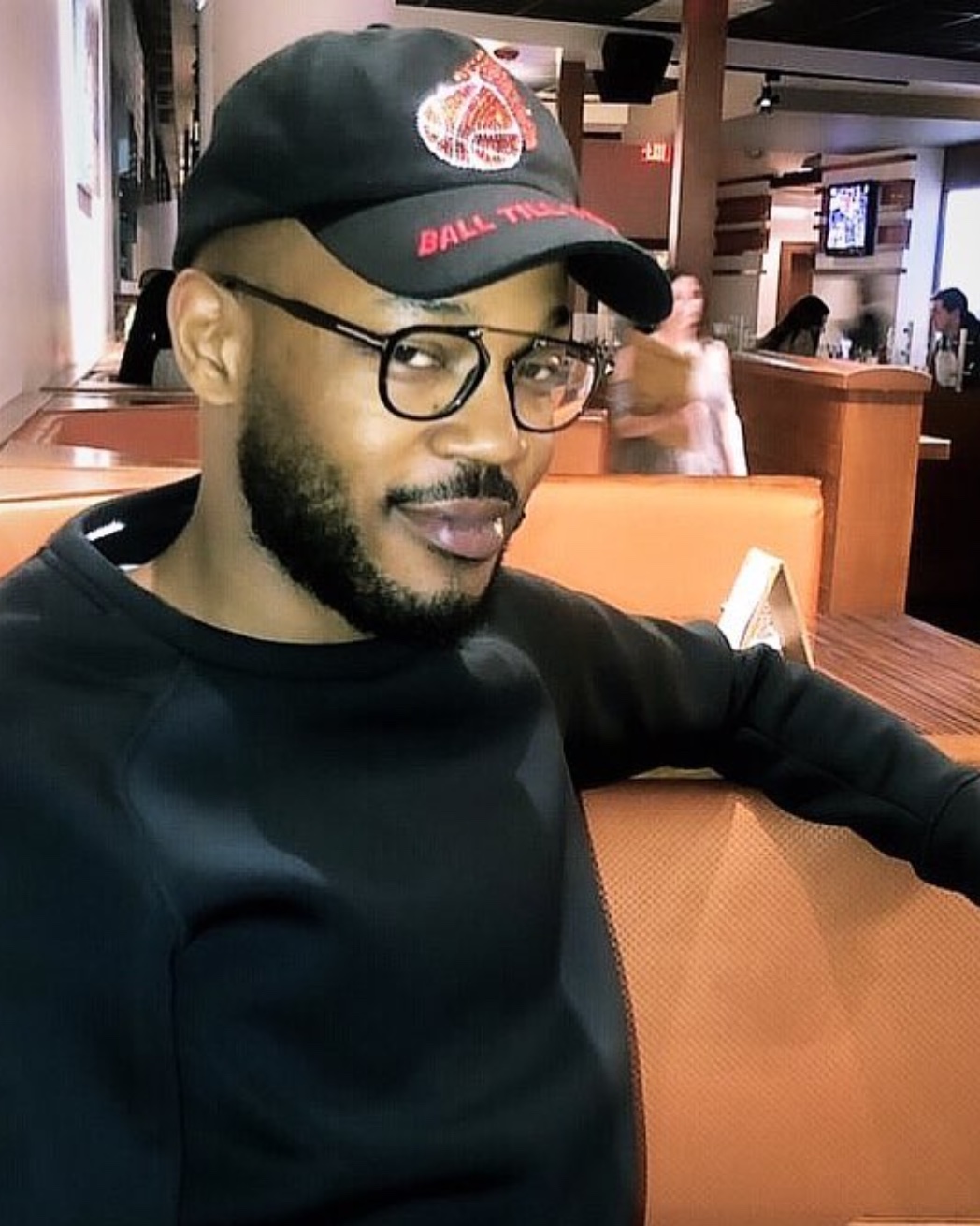 Hakeem Gaines in glasses and a black cap, seated in a restaurant booth