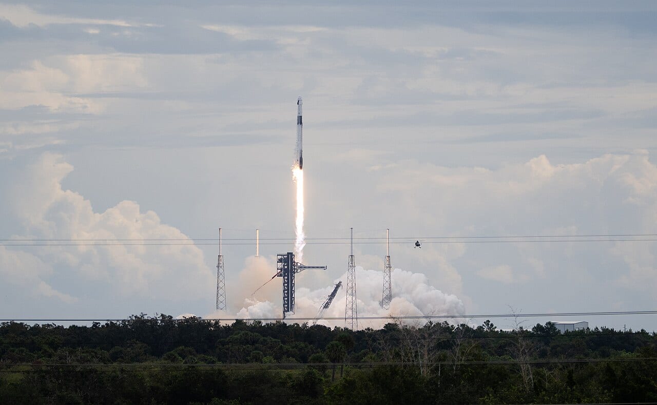 A SpaceX Falcon 9 rocket climbs away from its launch pad on NASA's Crew-13 mission, trailing smoke over the trees