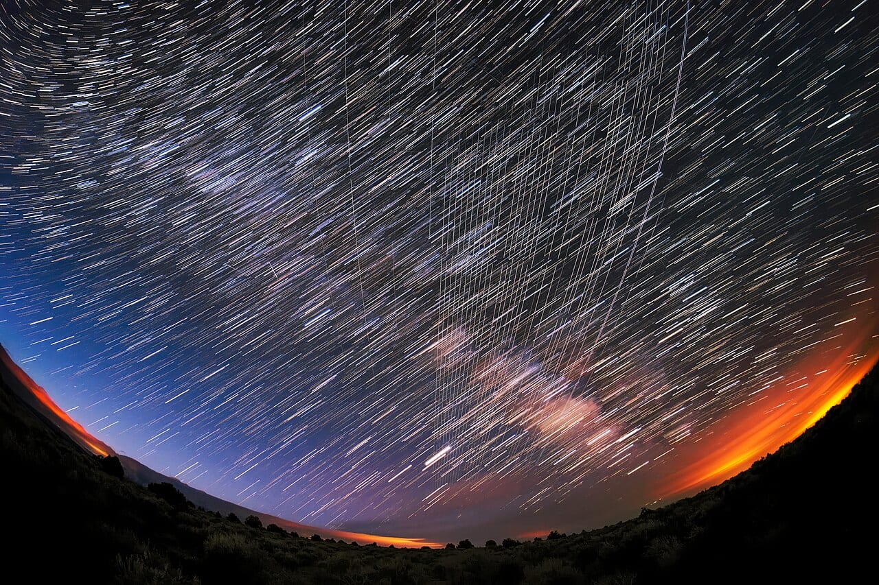 A long-exposure night sky of curved star trails crossed by the straight lines of Starlink satellites