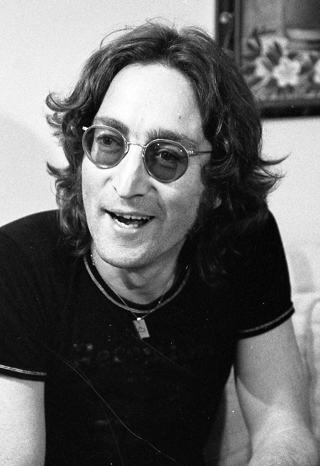 John Lennon in tinted round glasses, mid-sentence, in a black-and-white interview portrait