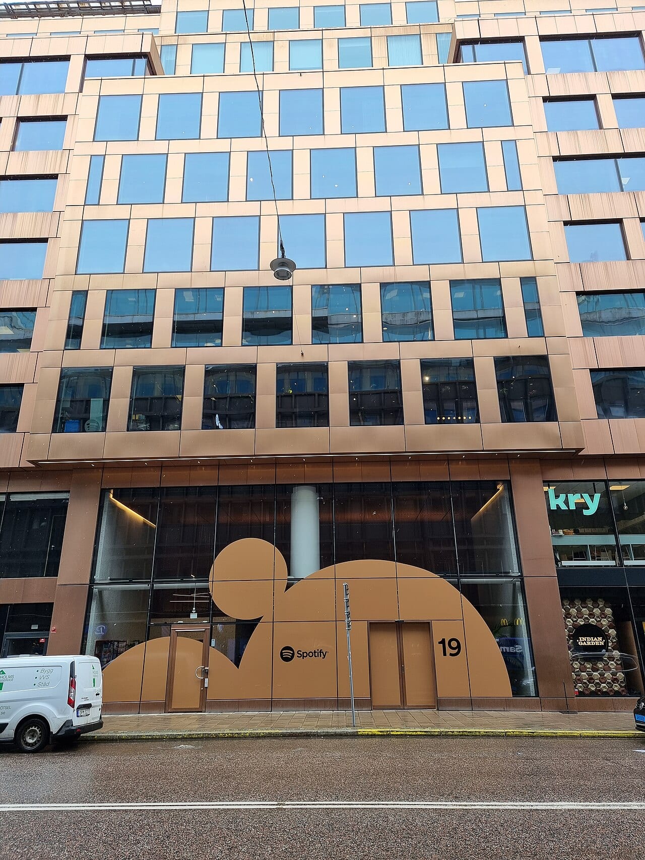 A copper-toned office facade in Stockholm with the Spotify logo and a large rounded orange shape across the ground-floor windows