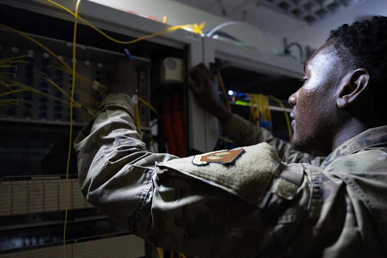 A U.S. Air Force technician checks a fiber optic connection inside a network switch cabinet