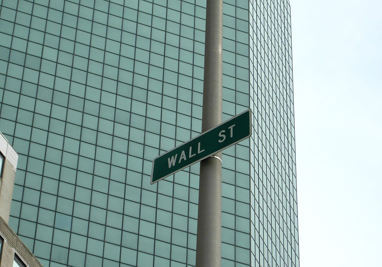 A green street sign reading Wall St against a clear sky in lower Manhattan